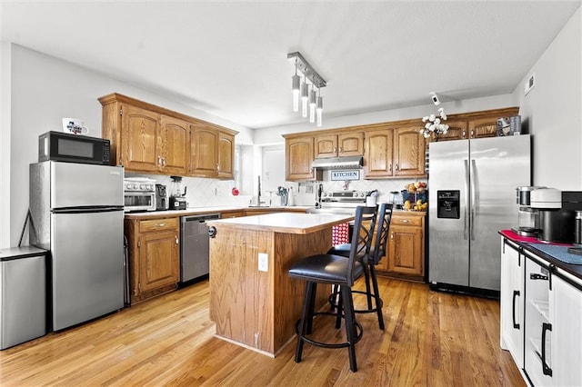 1005 Granada Dr, Raymore, MO 64083 - kitchen featuring stainless steel appliances, a kitchen island, light wood-style flooring, and tasteful backsplash