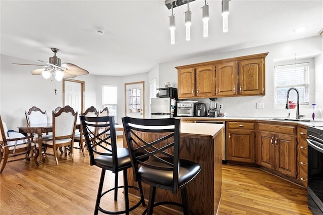 1005 Granada Dr, Raymore, MO 64083 - kitchen with a kitchen island, light wood-type flooring, a kitchen bar, brown cabinetry, and decorative backsplash