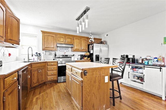 1005 Granada Dr, Raymore, MO 64083 - kitchen featuring stainless steel appliances, under cabinet range hood, a kitchen breakfast bar, light wood-style floors, and light countertops