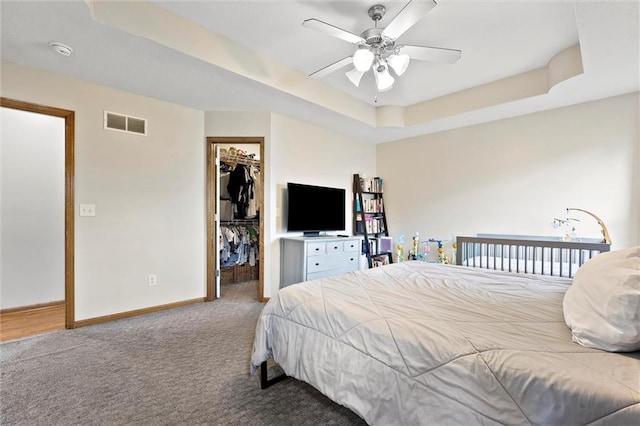 1005 Granada Dr, Raymore, MO 64083 - carpeted bedroom featuring a tray ceiling, a spacious closet, and a ceiling fan
