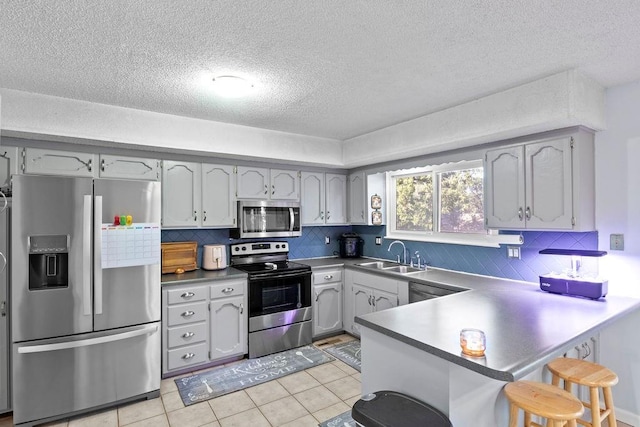 820 S Virginia Ln, Olathe, KS 66061 - kitchen featuring appliances with stainless steel finishes, a peninsula, decorative backsplash, a kitchen bar, and a textured ceiling
