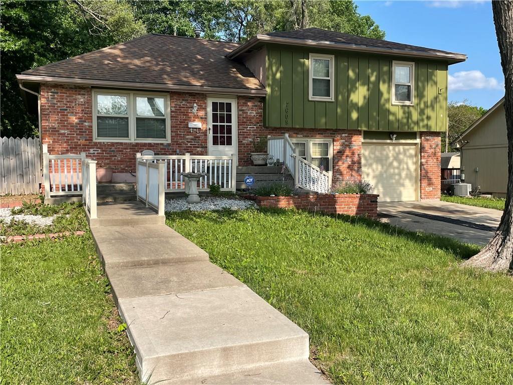 7609 Hayes St, Overland Park, KS 66204 - tri-level home with brick siding, an attached garage, board and batten siding, driveway, and roof with shingles