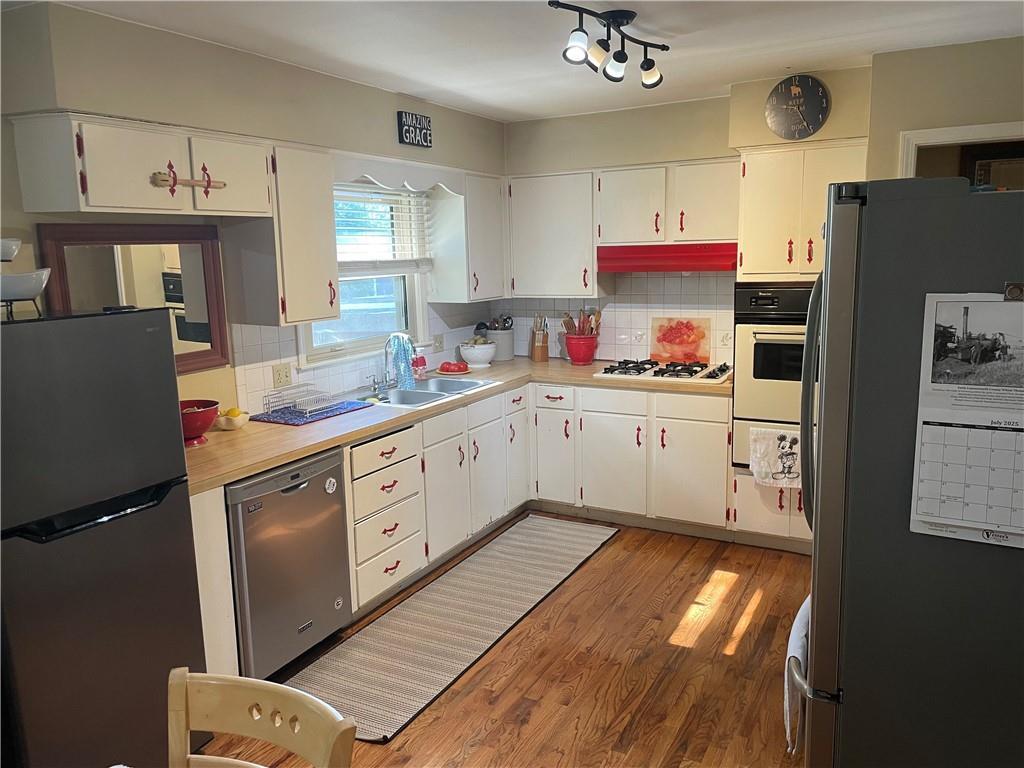 7609 Hayes St, Overland Park, KS 66204 - kitchen with appliances with stainless steel finishes, tasteful backsplash, light countertops, light wood-style floors, and white cabinets