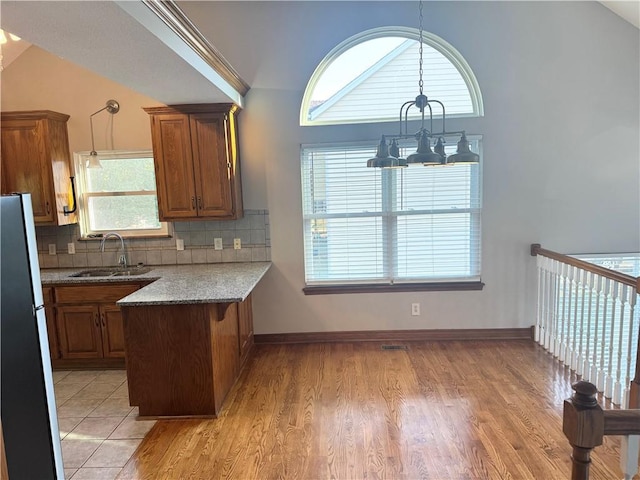 704 Canter St, Raymore, MO 64083 - kitchen with a chandelier, freestanding refrigerator, brown cabinetry, a peninsula, and plenty of natural light
