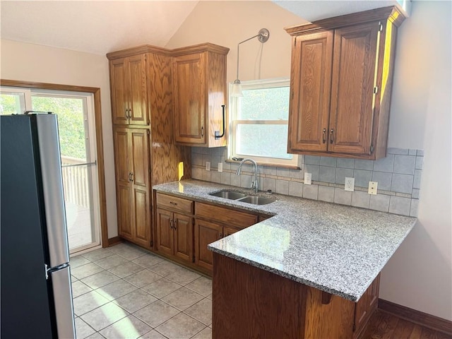 704 Canter St, Raymore, MO 64083 - kitchen featuring freestanding refrigerator, a peninsula, brown cabinets, decorative backsplash, and plenty of natural light
