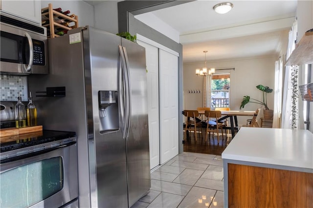 2026 E 70th Ter, Kansas City, MO 64132 - kitchen with appliances with stainless steel finishes, a chandelier, tasteful backsplash, crown molding, and hanging light fixtures