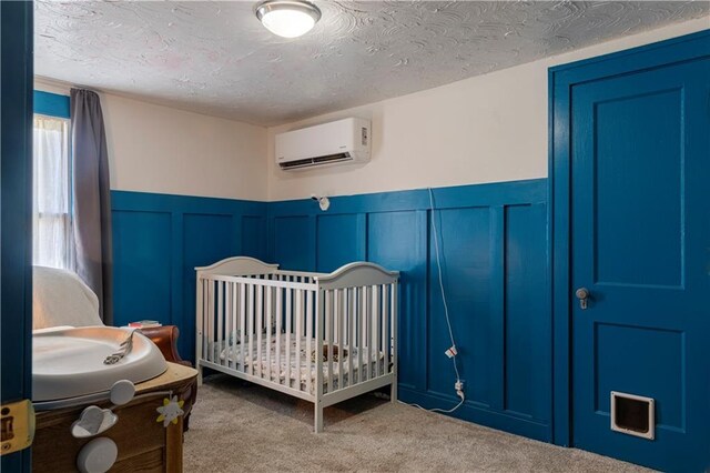 2026 E 70th Ter, Kansas City, MO 64132 - bedroom with a wall mounted air conditioner, carpet floors, a wainscoted wall, a textured ceiling, and a decorative wall