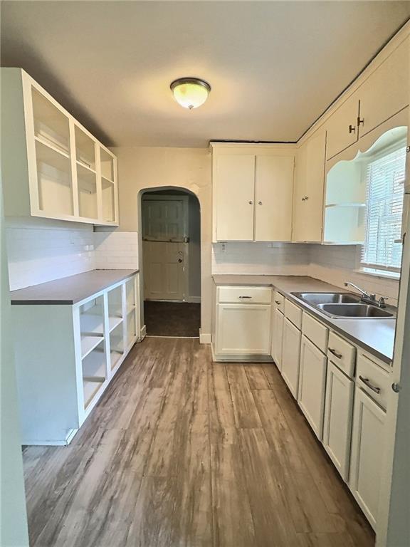 8409 Park Ave, Kansas City, MO 64132 - kitchen with open shelves, arched walkways, wood finished floors, white cabinetry, and tasteful backsplash