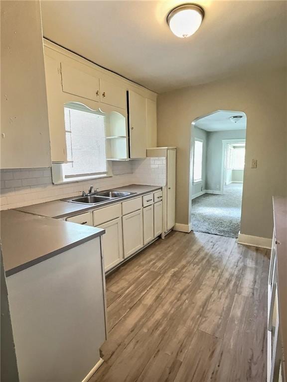 8409 Park Ave, Kansas City, MO 64132 - kitchen featuring arched walkways, decorative backsplash, white cabinets, and light wood finished floors