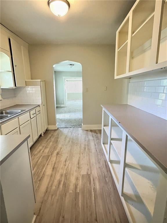 8409 Park Ave, Kansas City, MO 64132 - kitchen featuring arched walkways, tasteful backsplash, light wood-style flooring, white cabinetry, and open shelves