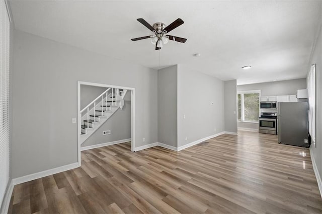 3543 Flora Ave, Kansas City, MO 64109 - unfurnished living room featuring stairway, ceiling fan, and light wood-style flooring