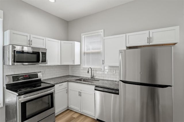 3543 Flora Ave, Kansas City, MO 64109 - kitchen featuring appliances with stainless steel finishes, white cabinetry, dark stone counters, tasteful backsplash, and light wood finished floors