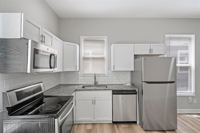 3543 Flora Ave, Kansas City, MO 64109 - kitchen featuring appliances with stainless steel finishes, white cabinets, light wood-style floors, and light stone countertops