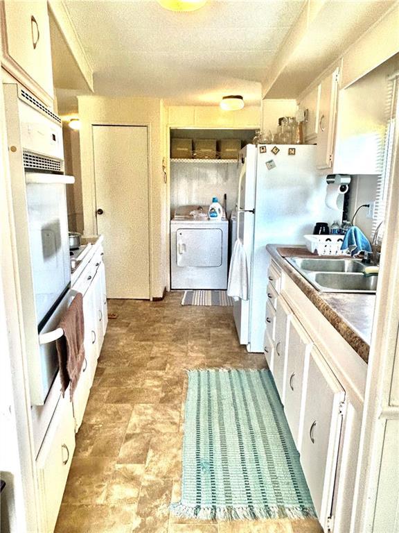 14444 E Quail Rd, Nevada, MO 64772 - kitchen with washer / clothes dryer, a warming drawer, white appliances, white cabinets, and a textured ceiling