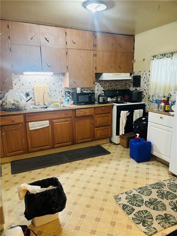 2506 S 48th Ter, Kansas City, KS 66106 - kitchen with exhaust hood, black microwave, white gas stove, decorative backsplash, and brown cabinetry