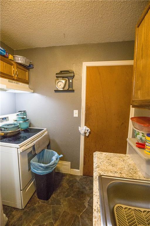5521-3 Wabash Ave, Kansas City, MO 64130 - kitchen with white range with electric cooktop, under cabinet range hood, brown cabinets, a textured ceiling, and light countertops