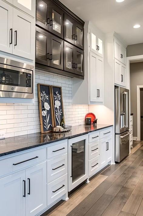 3409 W 187th St, Overland Park, KS 66085 - kitchen with appliances with stainless steel finishes, beverage cooler, wood finished floors, dark stone countertops, and glass insert cabinets