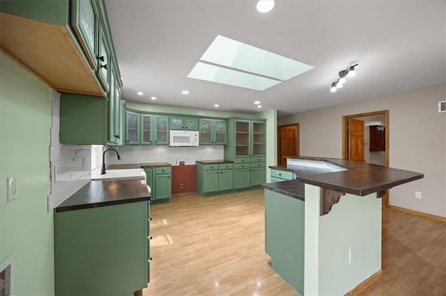 295 E 2300th Rd, Edgerton, KS 66021 - kitchen with green cabinetry, white microwave, dark countertops, a skylight, and light wood-style flooring