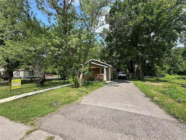 3009 N 33rd St, Kansas City, KS 66104 - bungalow-style house with driveway, covered porch, a front lawn, and view of wooded area