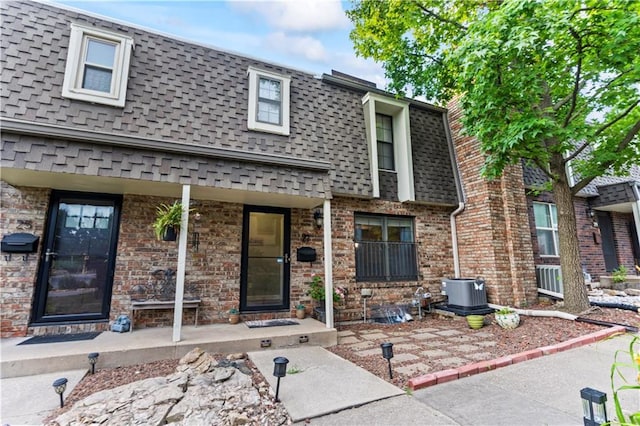 27 W Bannister Rd, Kansas City, MO 64114 - view of front of house featuring mansard roof, roof with shingles, a porch, and brick siding