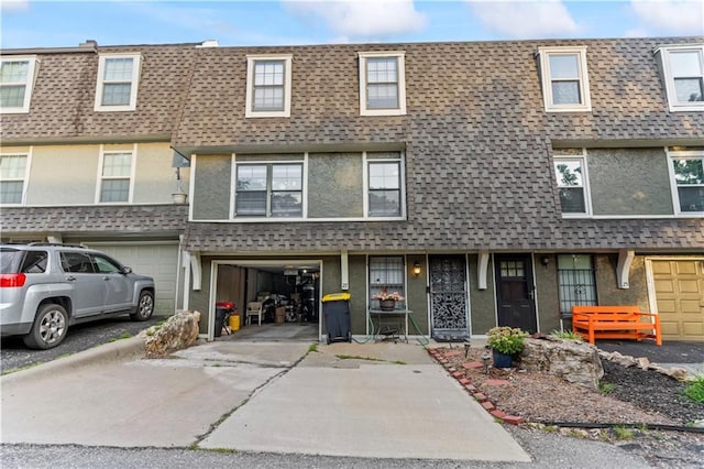 27 W Bannister Rd, Kansas City, MO 64114 - view of property featuring roof with shingles, mansard roof, an attached garage, driveway, and stucco siding