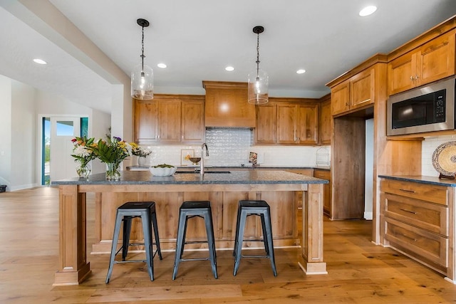 2416 W 177th St, Overland Park, KS 66085 - kitchen with stainless steel microwave, brown cabinets, custom range hood, recessed lighting, and a kitchen breakfast bar