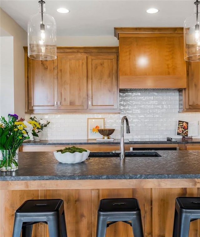 2416 W 177th St, Overland Park, KS 66085 - kitchen with brown cabinets, a breakfast bar, backsplash, custom range hood, and pendant lighting