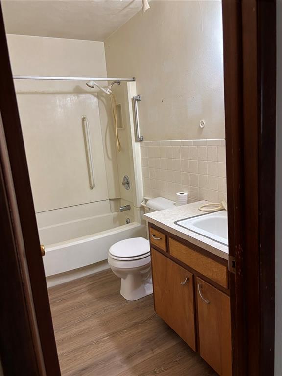 420 S Walnut St, Iola, KS 66749 - bathroom with tile walls, vanity, bathing tub / shower combination, wood finished floors, and wainscoting