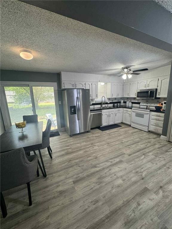 213 SW Palo Dr, Blue Springs, MO 64014 - kitchen featuring stainless steel appliances, white cabinets, dark countertops, ceiling fan, and wood finished floors