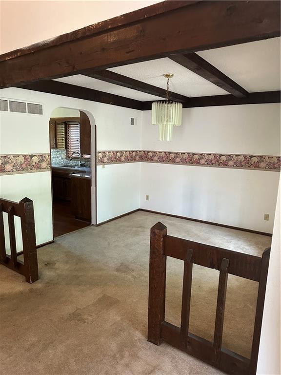 7908 E 96th St, Kansas City, MO 64134 - spare room with arched walkways, beam ceiling, a chandelier, and carpet floors