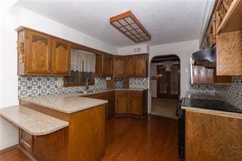 7908 E 96th St, Kansas City, MO 64134 - kitchen with a peninsula, decorative backsplash, light countertops, arched walkways, and brown cabinets