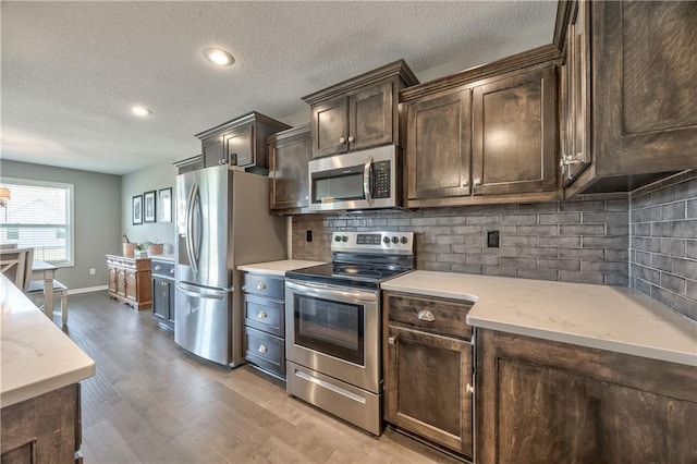 4246 Lakeview Ter, Basehor, KS 66007 - kitchen with stainless steel appliances, dark brown cabinets, light wood finished floors, a textured ceiling, and backsplash