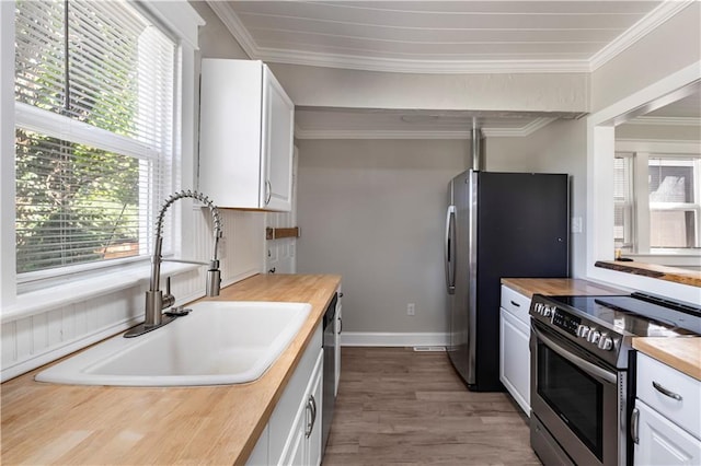 4001 Tracy Ave, Kansas City, MO 64110 - kitchen with stainless steel appliances, wooden counters, white cabinetry, crown molding, and wood finished floors