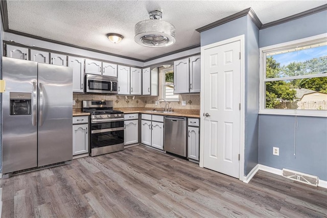 2005 Manor Pl, Blue Springs, MO 64015 - kitchen featuring stainless steel appliances, ornamental molding, dark wood-type flooring, backsplash, and a textured ceiling