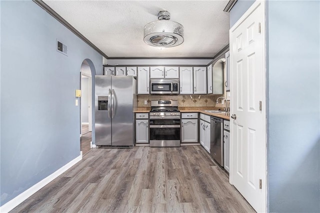 2005 Manor Pl, Blue Springs, MO 64015 - kitchen with appliances with stainless steel finishes, arched walkways, dark wood-style floors, ornamental molding, and backsplash