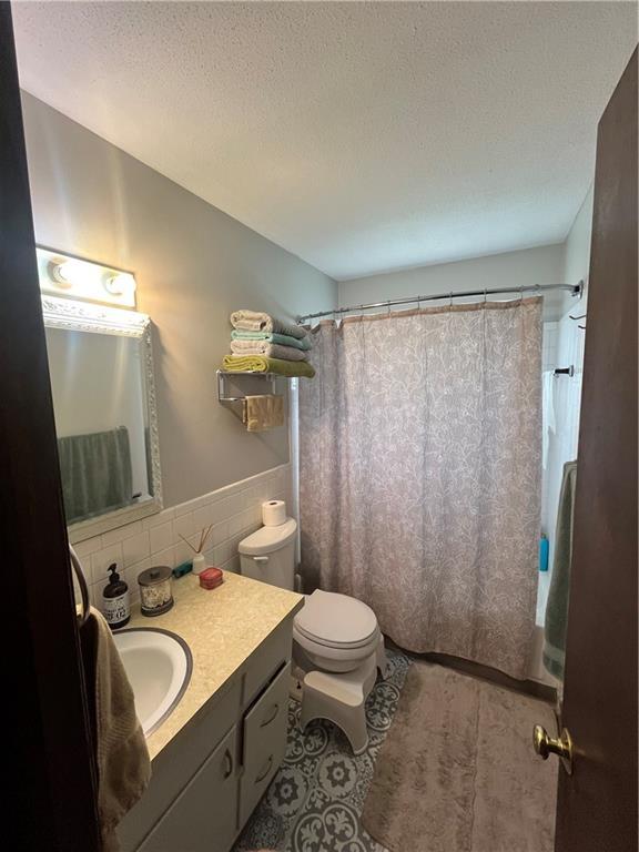 1835-1837 N 77th St, Kansas City, KS 66112 - full bath featuring vanity, tile walls, a textured ceiling, wainscoting, and tile patterned flooring