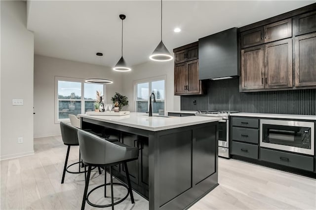 18221 W 168th Ter, Olathe, KS 66062 - kitchen with appliances with stainless steel finishes, wall chimney exhaust hood, light countertops, light wood finished floors, and a kitchen island with sink