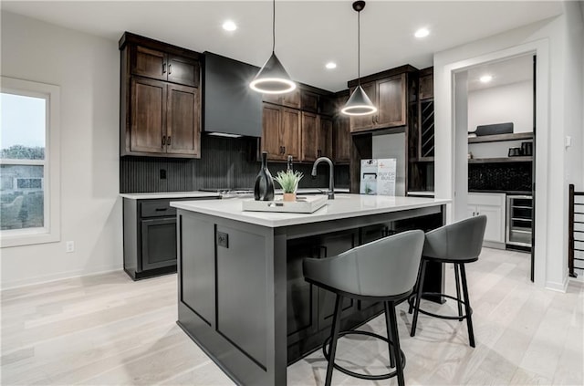 18221 W 168th Ter, Olathe, KS 66062 - kitchen featuring wine cooler, wall chimney exhaust hood, backsplash, light countertops, and light wood-style flooring
