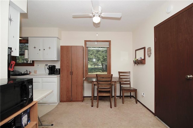 414 N Ash St, Garnett, KS 66032 - kitchen featuring black microwave, light countertops, light carpet, white cabinetry, and ceiling fan