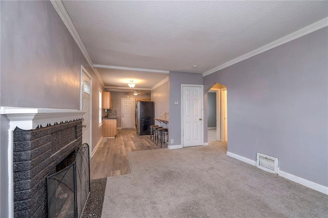 904 E 84th St, Kansas City, MO 64131 - unfurnished living room featuring a brick fireplace, ornamental molding, light colored carpet, arched walkways, and a textured ceiling