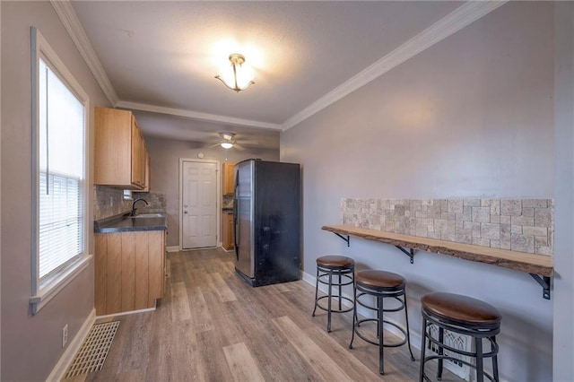 904 E 84th St, Kansas City, MO 64131 - kitchen with freestanding refrigerator, a kitchen breakfast bar, backsplash, light wood finished floors, and crown molding