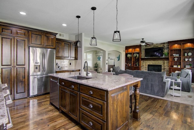 16324 S Locust St, Olathe, KS 66062 - kitchen with appliances with stainless steel finishes, ceiling fan, a stone fireplace, dark wood-style floors, and arched walkways