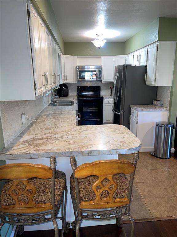 177 1150th St, Humboldt, KS 66748 - kitchen with black / electric stove, stainless steel microwave, light countertops, a peninsula, and freestanding refrigerator