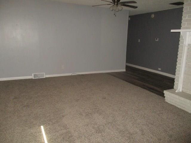 unfurnished living room with a fireplace, dark colored carpet, and ceiling fan