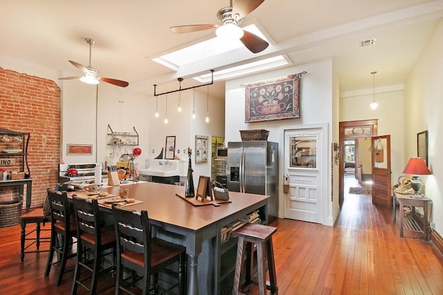 kitchen with ceiling fan, stainless steel fridge, wood-type flooring, brick wall, and a breakfast bar area