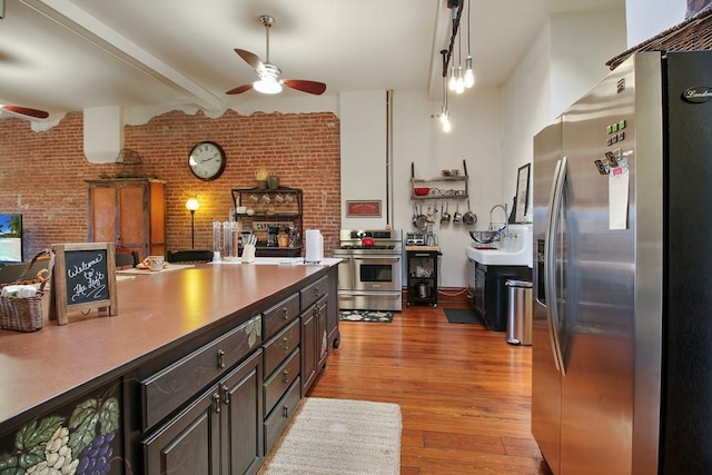 kitchen featuring ceiling fan, hardwood / wood-style floors, brick wall, and appliances with stainless steel finishes