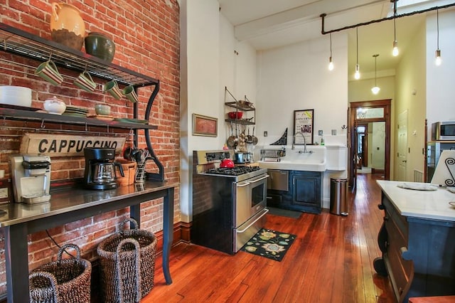 kitchen featuring blue cabinetry, decorative light fixtures, dark hardwood / wood-style flooring, brick wall, and appliances with stainless steel finishes