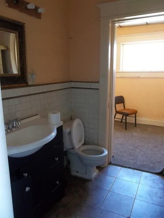 bathroom featuring tile flooring, vanity, toilet, and tile walls