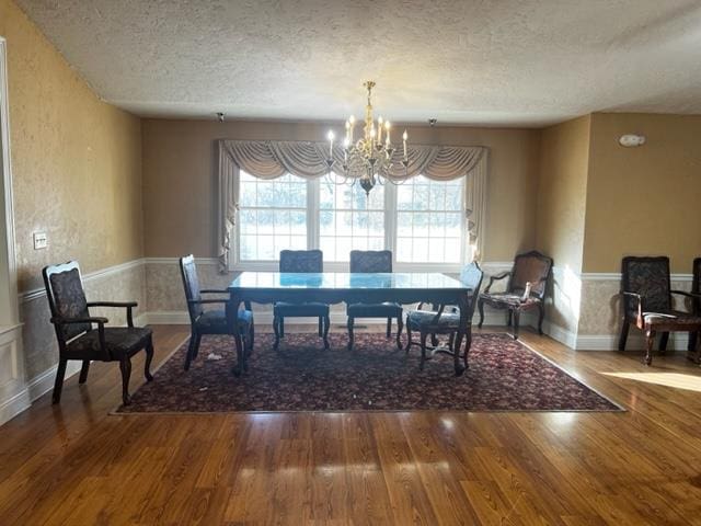 dining space with baseboards, wood finished floors, a textured ceiling, and a notable chandelier