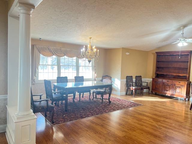 dining room featuring a textured ceiling, decorative columns, ceiling fan with notable chandelier, hardwood / wood-style flooring, and vaulted ceiling